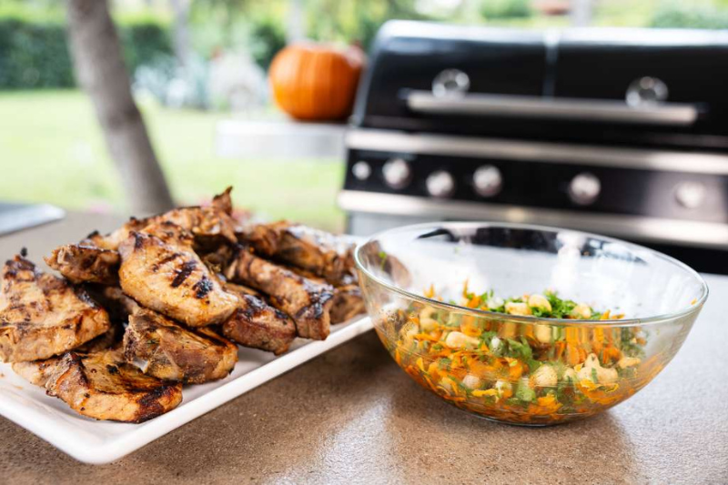 Χοιρινές μπριζόλες στη σχάρα με μαρινάδα εσπεριδοειδών και καροτοσαλάτα, σερβιρισμένες δίπλα σε ψησταριά Outdoorchef.